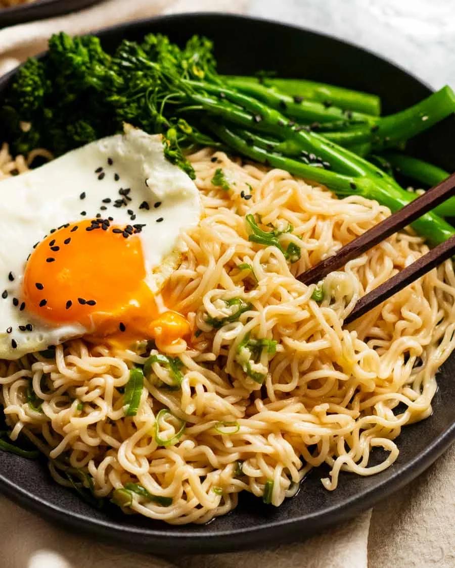 Noodles with a fried egg and greens on a black plate
